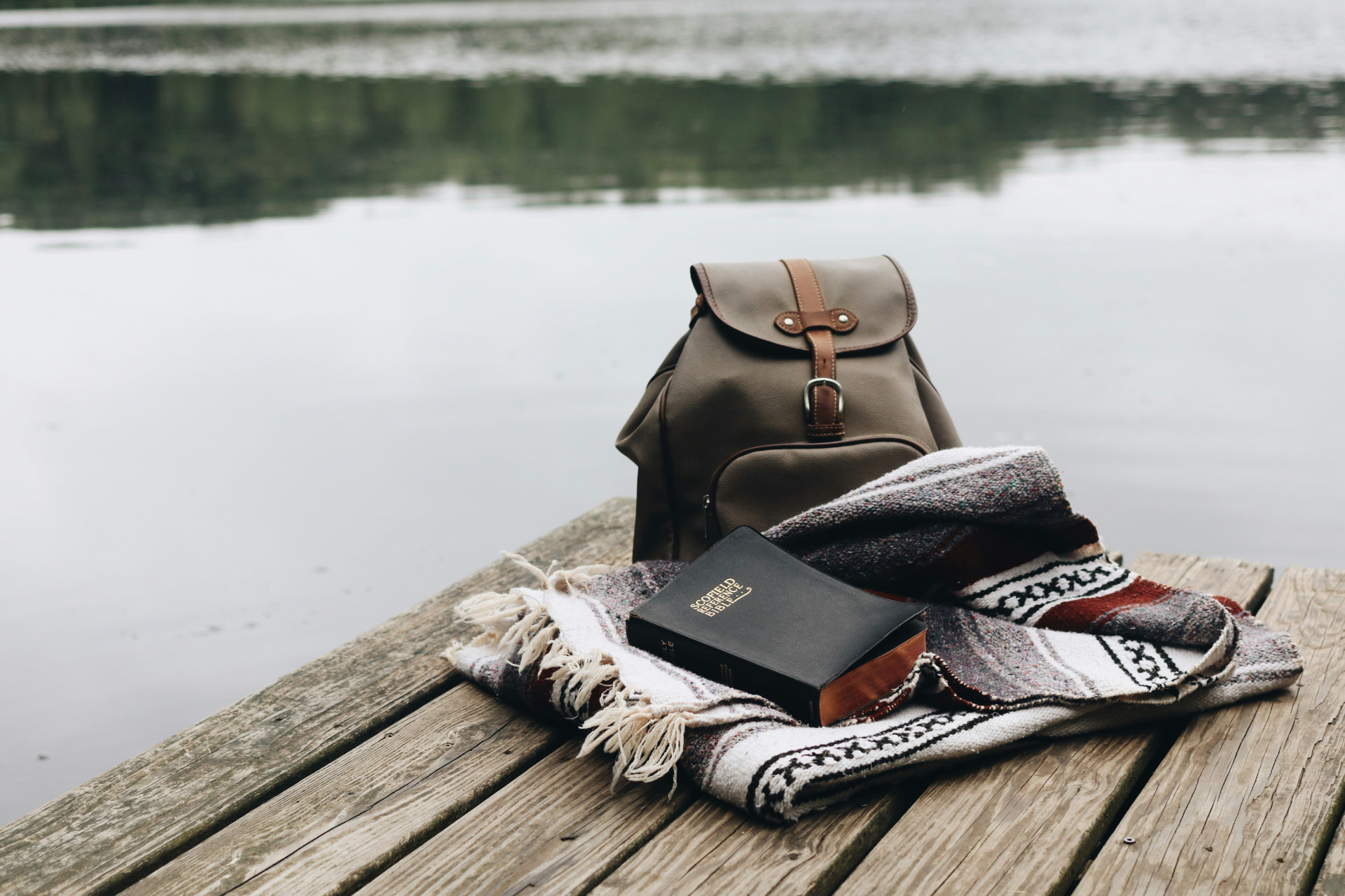 A backpack, blanket and book resting on a wooden jetty by a still lake